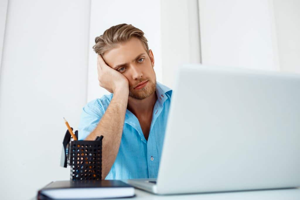 young handsome tired confident pensive businessman sitting table working laptop with cup coffee aside white modern office interior